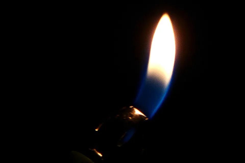 Choosing a Cigar Lighter — tall yellow and blue lighter flame glowing against a pure black background