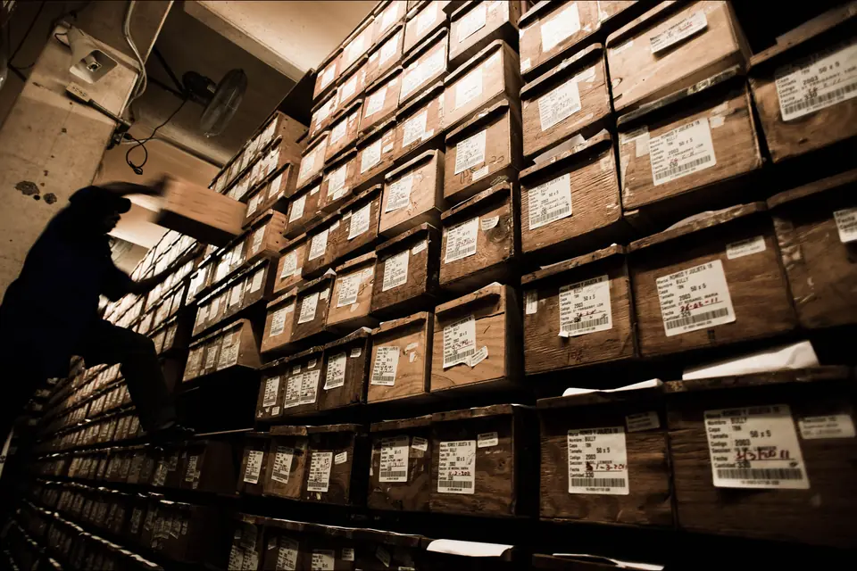 Cigar Sizes: Size Chart, Ring Gauge and Vitolas Explained — stacked cedar cigar boxes ageing on shelves in a dark factory storeroom