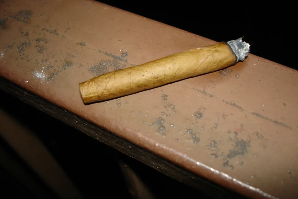 Choosing a Cigar Ashtray — burning cigarillo with a short tip of grey ash resting on a wooden rail