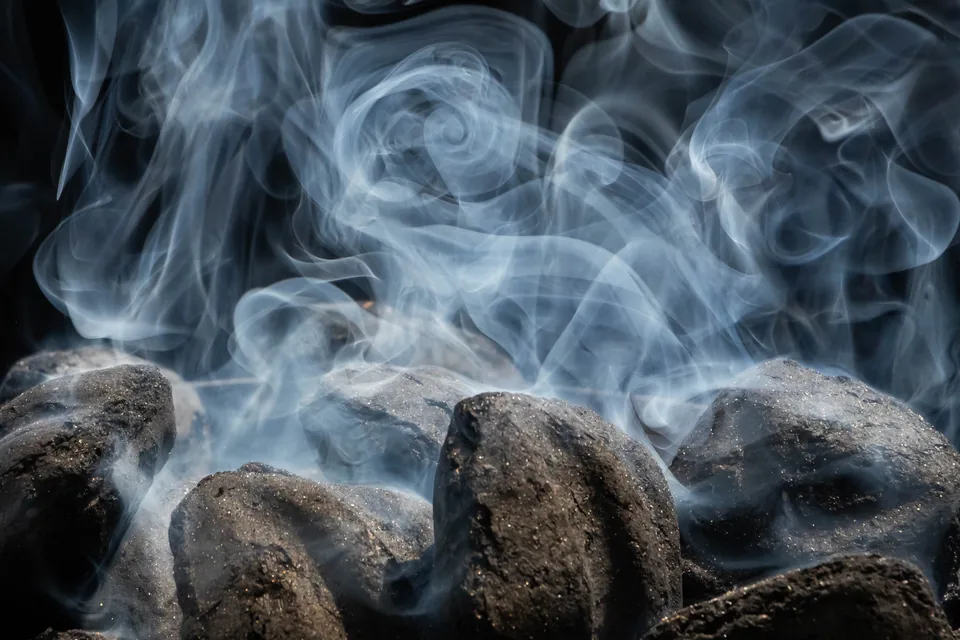 Do You Inhale Cigars? No, and Here Is Why — pale blue wisps of smoke swirling above dark smouldering coals