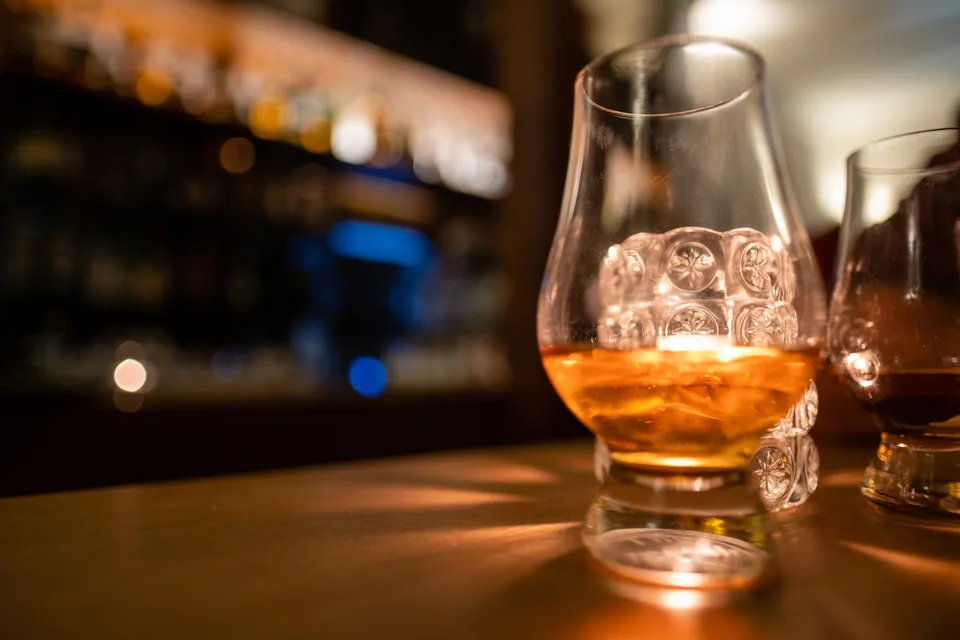 Cigar Pairing Guide — nosing glass of amber whisky on a dark bar with warm bottles behind