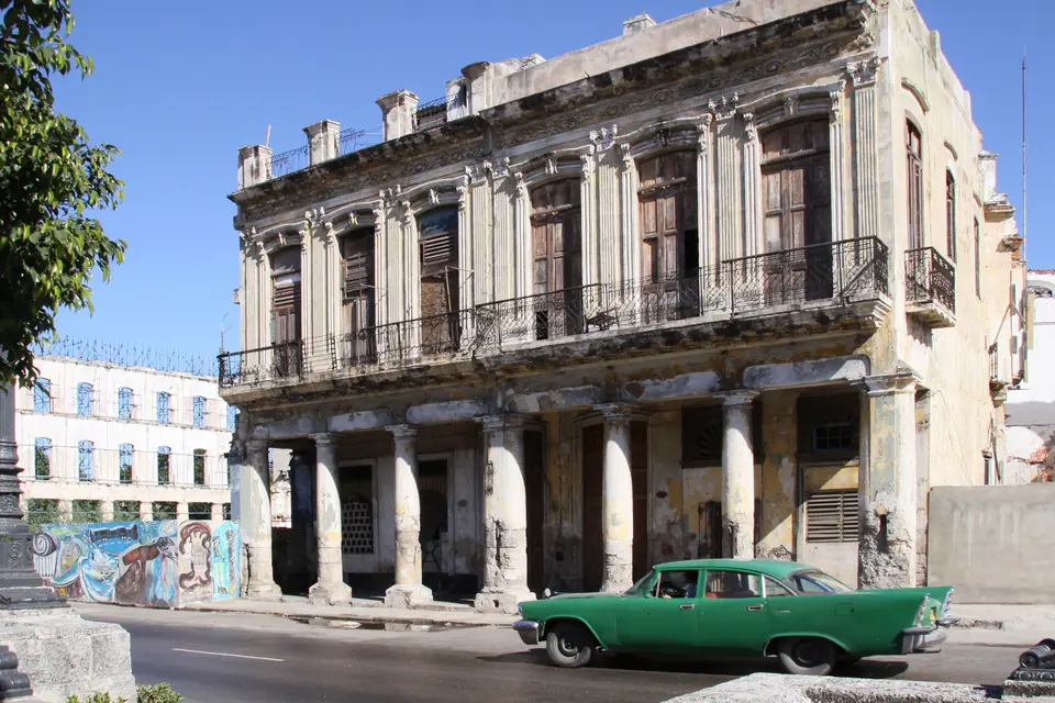 Partagás (Partagas Cigar): Brand Profile — green classic American car passing a weathered colonial building on a Havana street